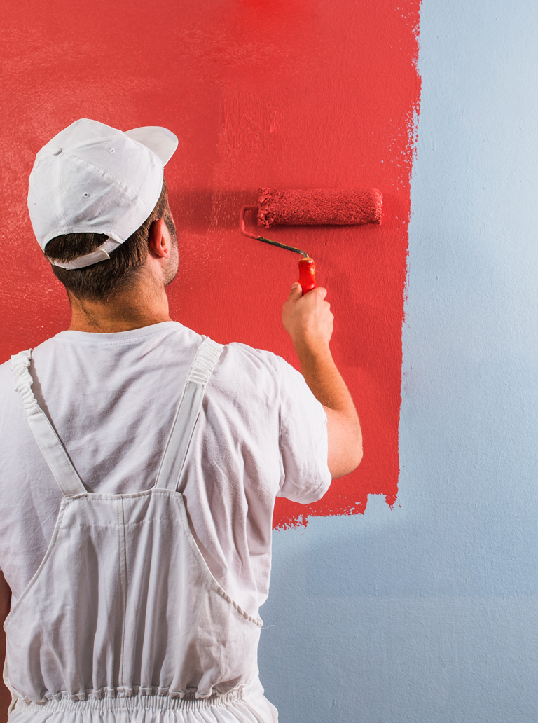 Professional painter applying red paint on interior wall using roller during accent wall design project.