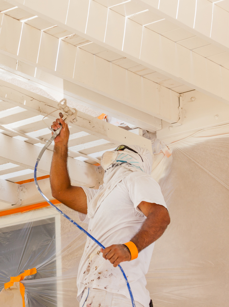 Professional painter using spray equipment to paint industrial ceiling beams