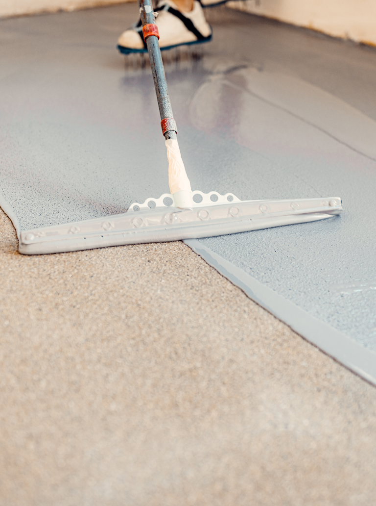 Worker spreading grey epoxy floor coating with trowel