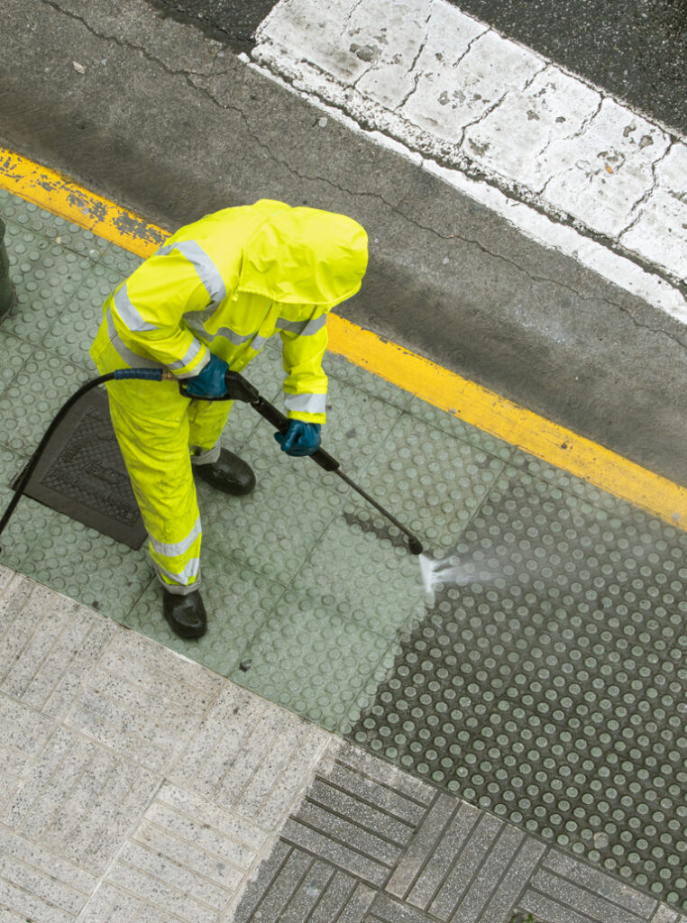 Worker performing sidewalk pressure washing in Ottawa wearing safety gear