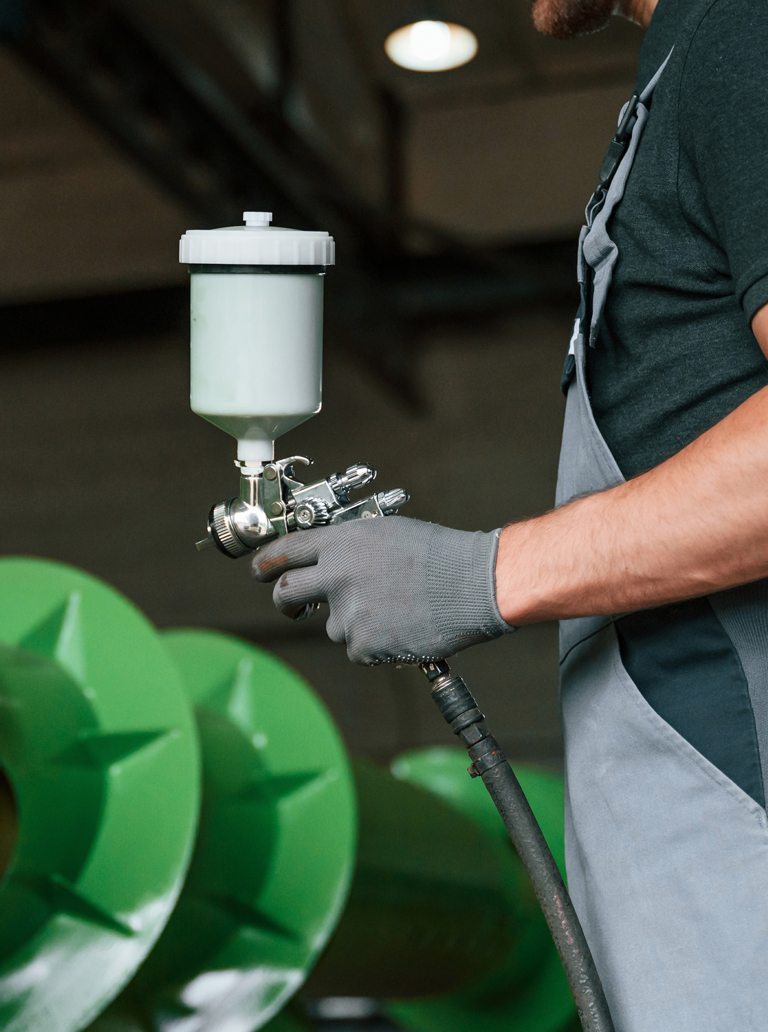 Industrial worker using spray gun to paint metal parts in factory