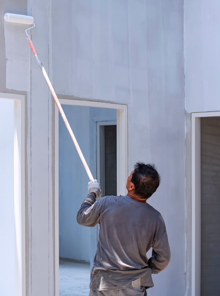 Painter applying white paint to a new drywall wall using an extension roller during interior construction in Ontario.