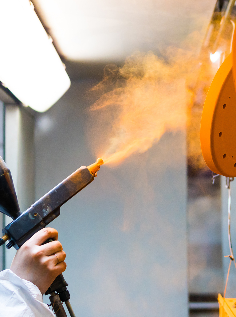 Technician applying powder coating on industrial metal part