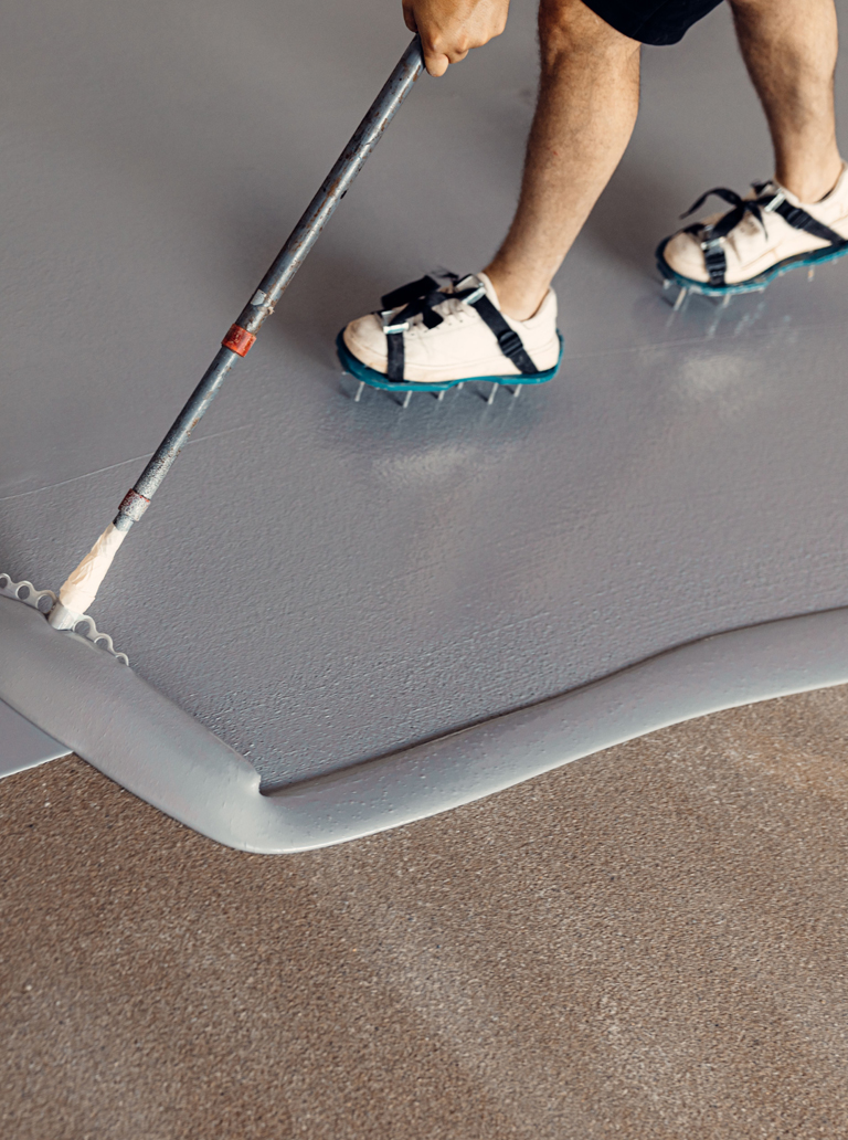Worker applying grey epoxy floor coating with roller