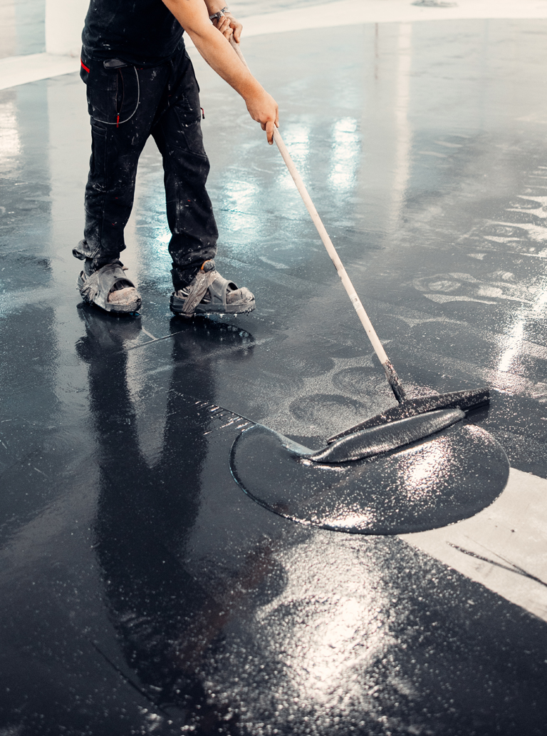 Worker applying industrial epoxy coating on concrete floor