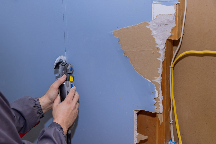 Contractor cutting and removing damaged drywall section for wall repair