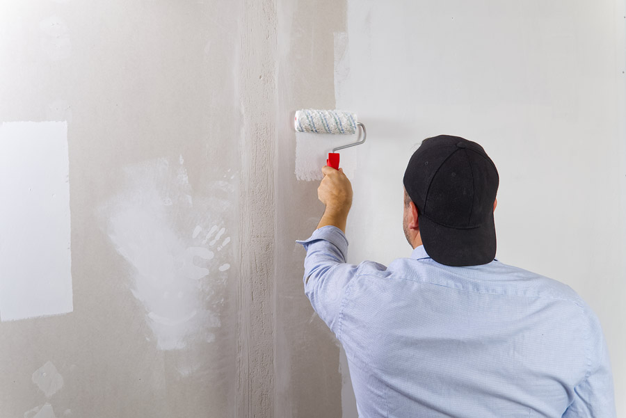 Painter applying primer on repaired drywall using roller brush
