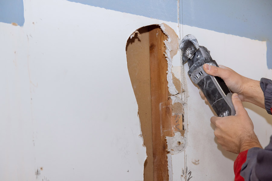Professional drywall repair with cutting tool removing damaged wall section