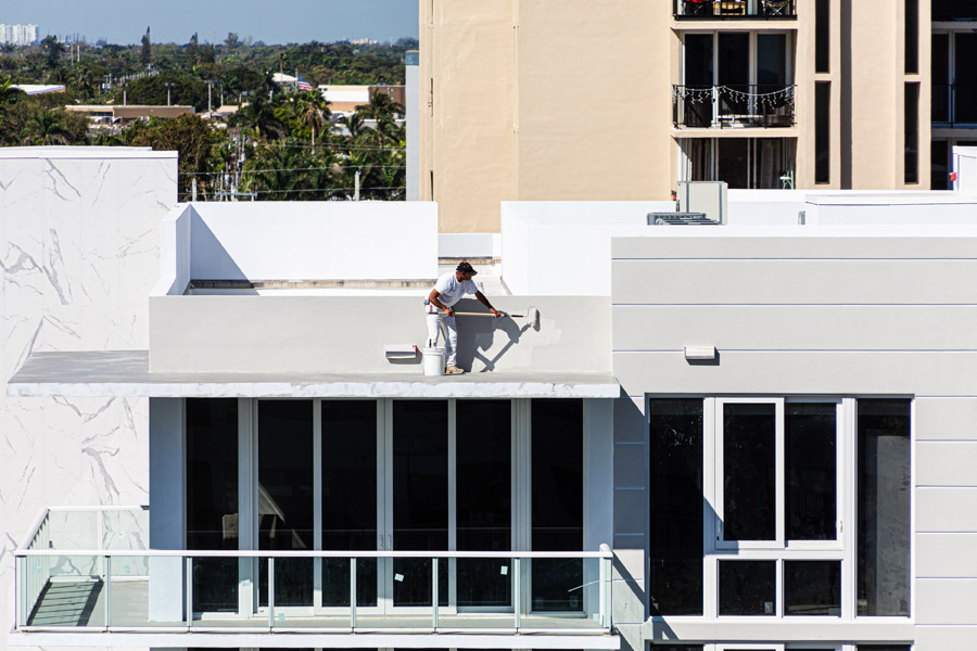 Professional painter applying exterior coating on modern building rooftop