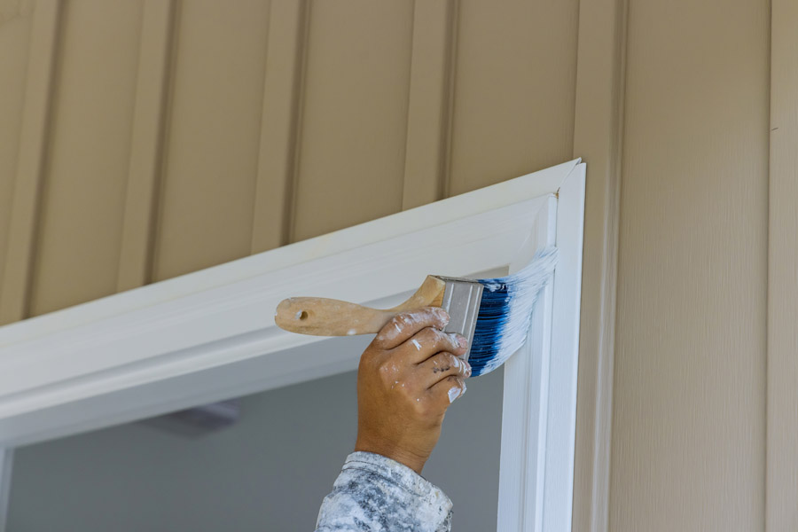 Painter applying white paint on exterior window trim with brush